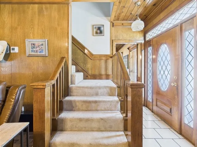 Foyer featuring stairs, light tile patterned flooring, wood walls, and wooden ceiling