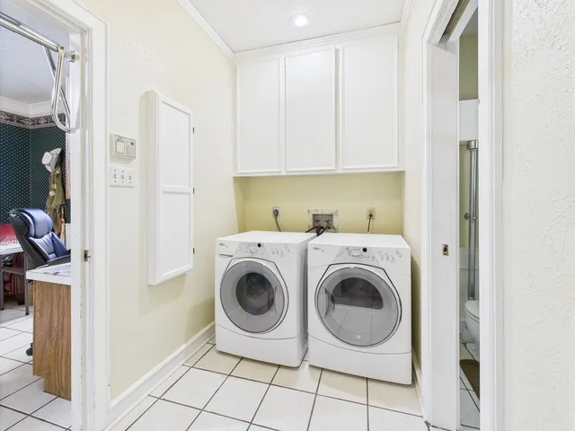 Washroom with washing machine and dryer, light tile patterned flooring, crown molding, and cabinet space