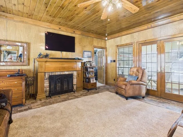 Carpeted living room with wood ceiling, a ceiling fan, a fireplace, wooden walls, and crown molding