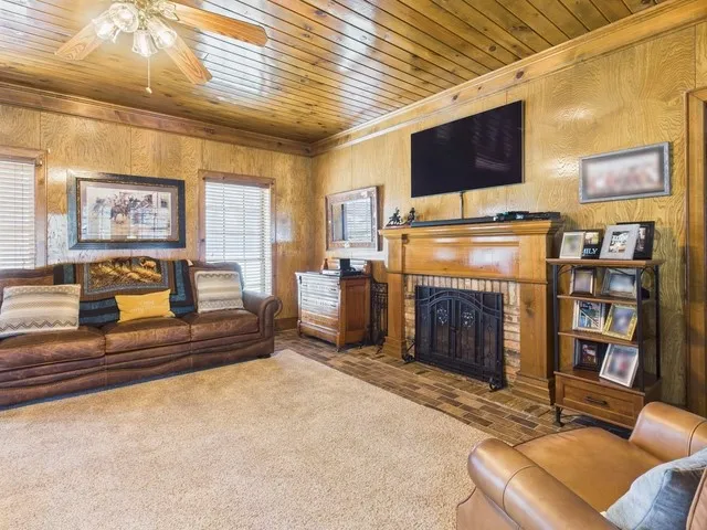 Living area featuring wooden ceiling, crown molding, a fireplace, ceiling fan, and wood walls