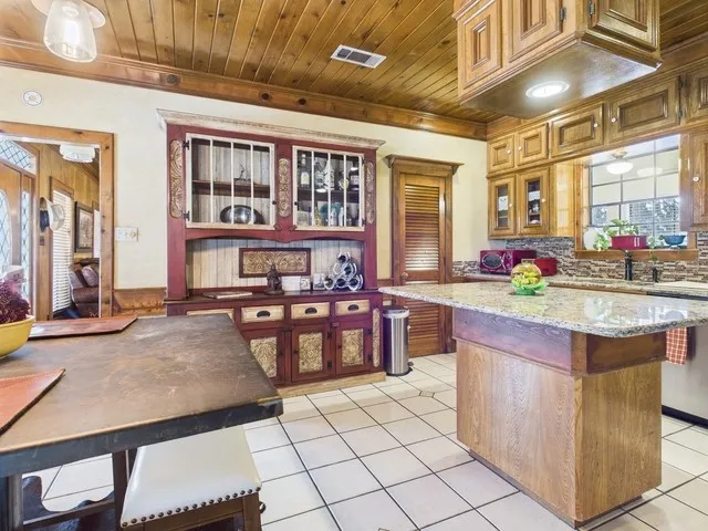Kitchen featuring wooden ceiling, a kitchen island, light tile patterned flooring, stainless steel dishwasher, and glass insert cabinets
