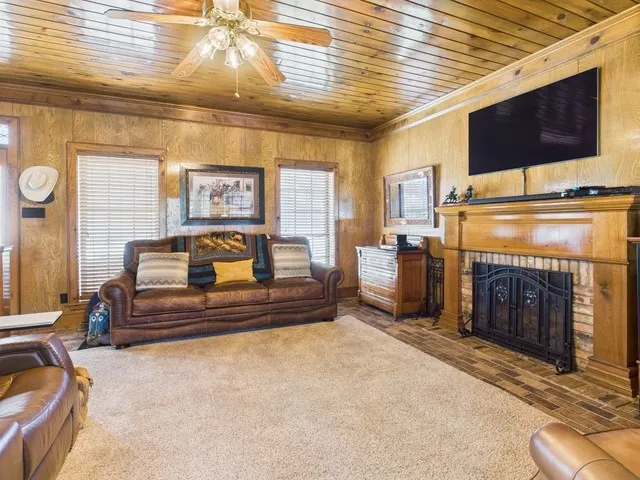 Living room featuring wooden ceiling, ornamental molding, wooden walls, a ceiling fan, and a fireplace