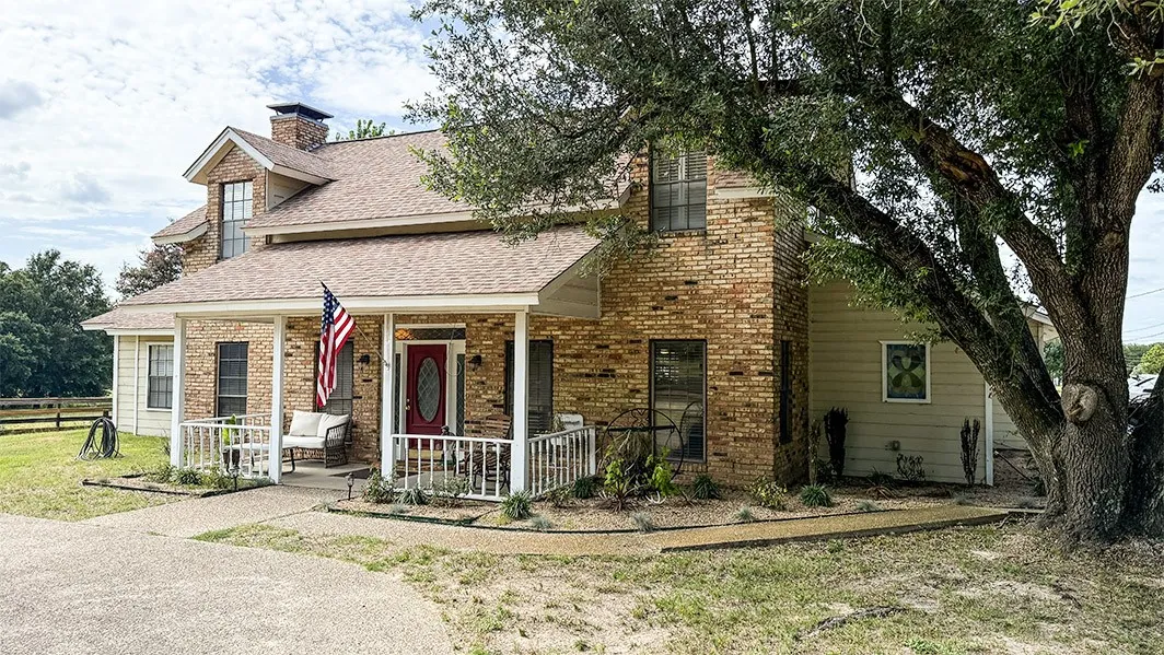 View of front of home featuring a chimney, a shingled roof, brick siding, and a porch
