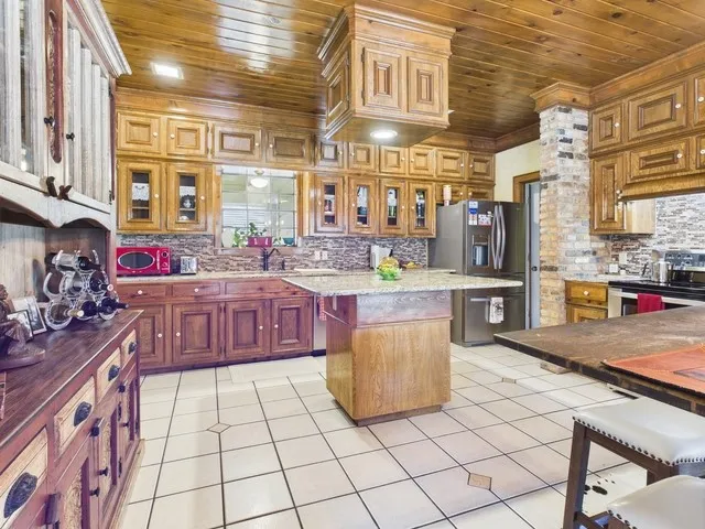 Kitchen with wooden ceiling, appliances with stainless steel finishes, tasteful backsplash, a kitchen island, and ornamental molding