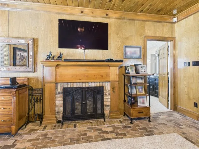 Detailed view of a fireplace, crown molding, wooden ceiling, and wood walls