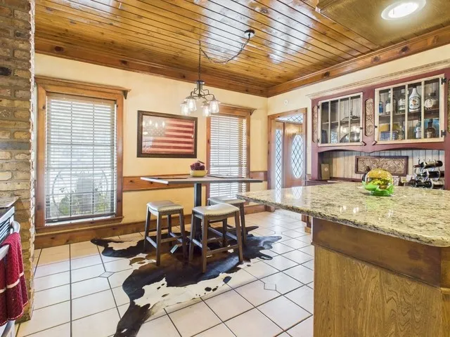 Kitchen with light tile patterned floors, wood ceiling, decorative light fixtures, a chandelier, and glass insert cabinets