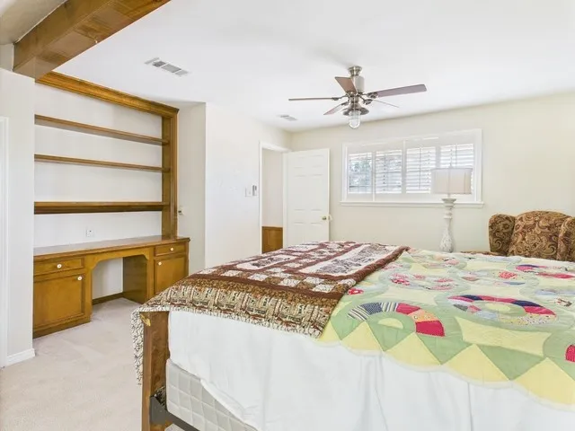Bedroom with light carpet, built in study area, and a ceiling fan
