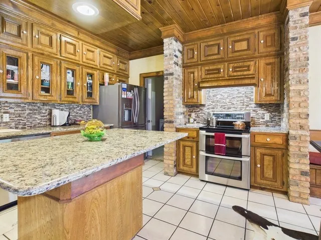 Kitchen featuring appliances with stainless steel finishes, wood ceiling, light tile patterned flooring, backsplash, and brown cabinetry