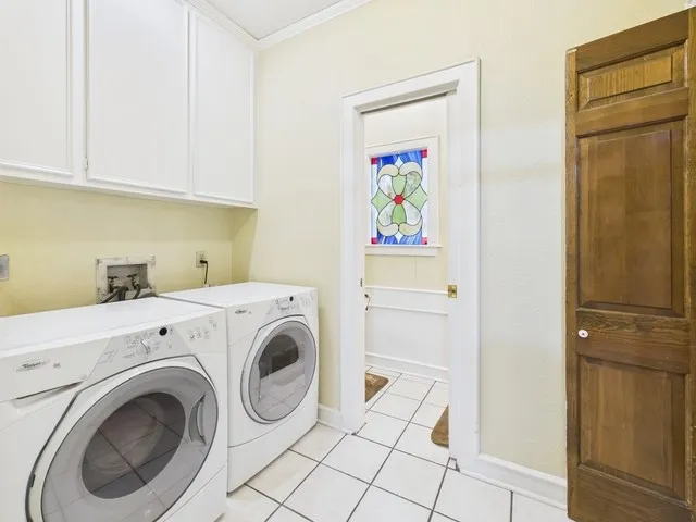 Laundry area with cabinet space, washer and dryer, ornamental molding, and light tile patterned flooring