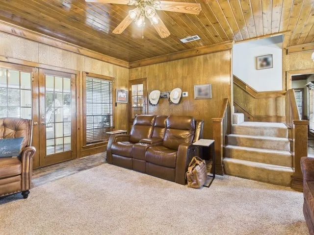 Carpeted living area with wooden ceiling, wood walls, ceiling fan, and stairway