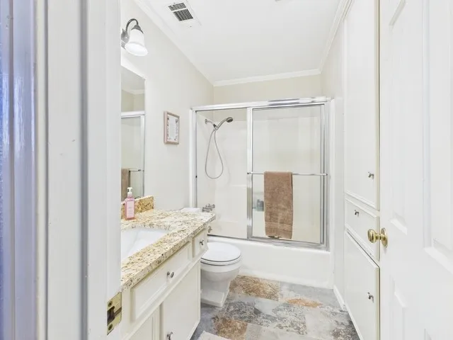 Full bath with vanity, combined bath / shower with glass door, crown molding, and stone finish floors