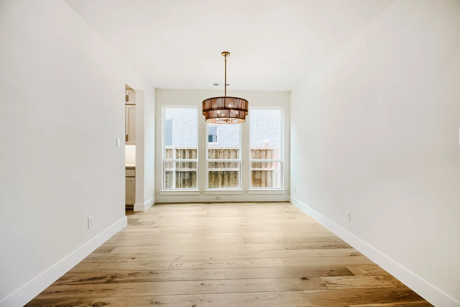 Dining area featuring a contemporary chandelier, three large windows, light wood-finish flooring, and white baseboards
