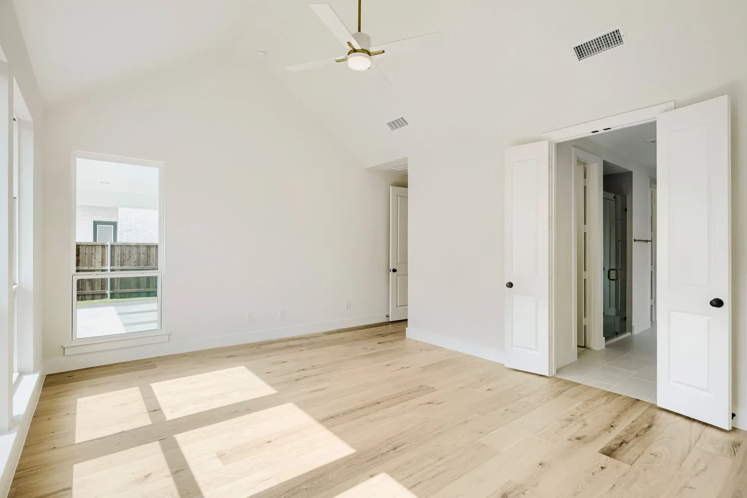 Spacious interior room featuring a vaulted ceiling with a modern ceiling fan, wood-finish flooring, and bright white walls