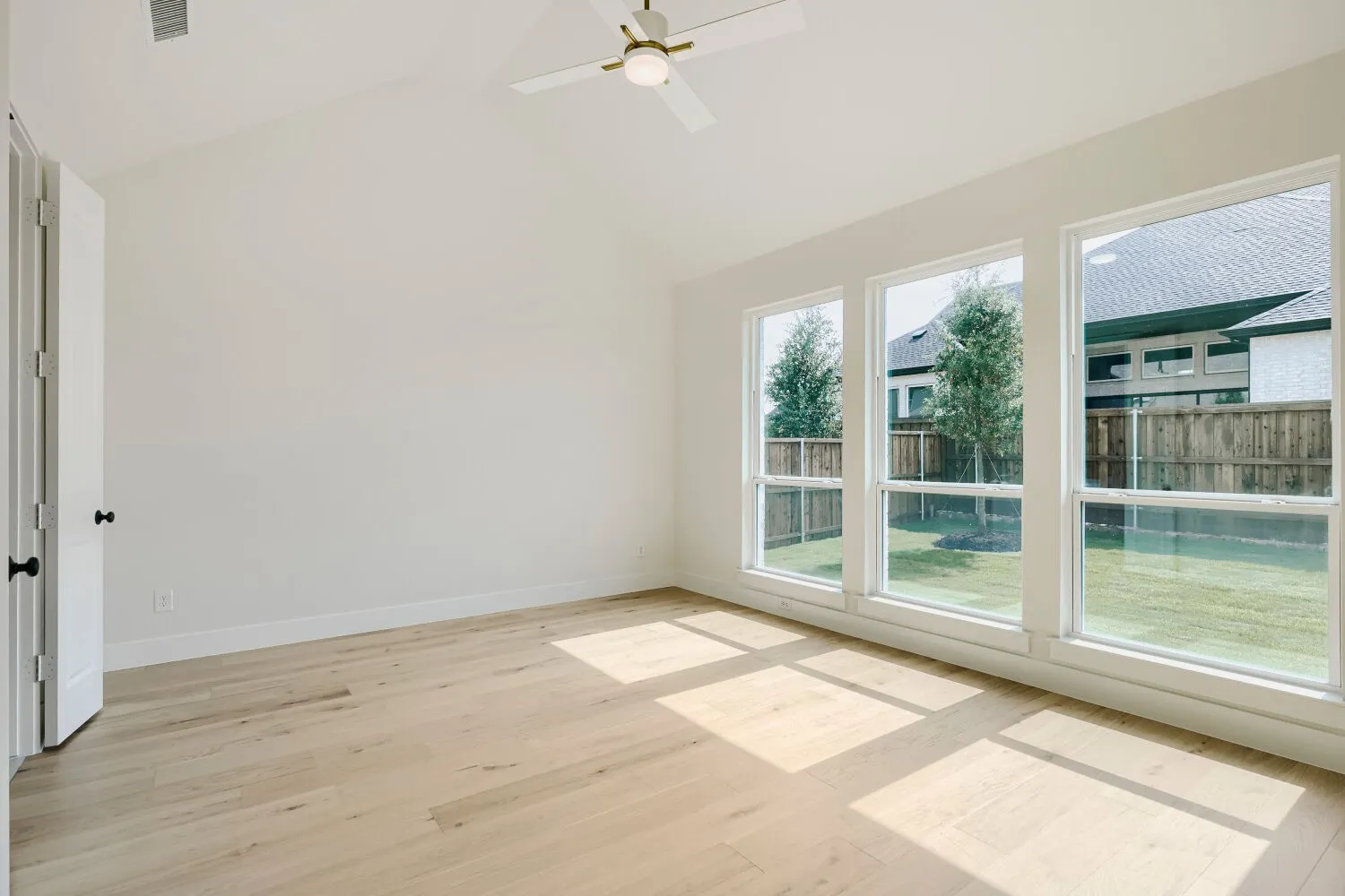 Vaulted ceiling room featuring light wood-finish flooring, three vertical windows, and a ceiling fan with integrated lighting