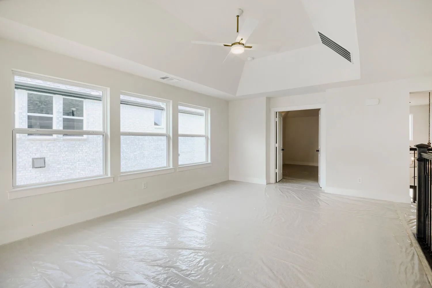 Spacious room featuring a vaulted ceiling with a modern ceiling fan, three large windows, white trim, and a doorway opening to an interior space