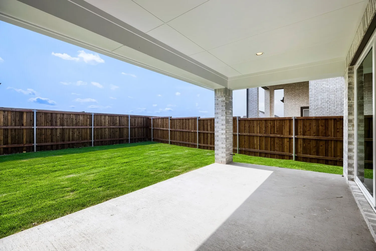 Expansive outdoor living area featuring a covered concrete patio, a spacious lawn, and a privacy fence