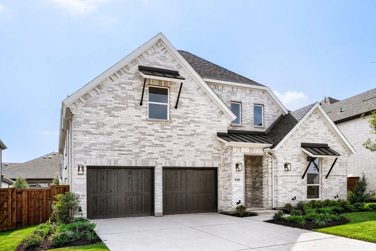 Contemporary two-story residence featuring a light-colored brick facade, dark wood-finish garage doors, and a concrete driveway