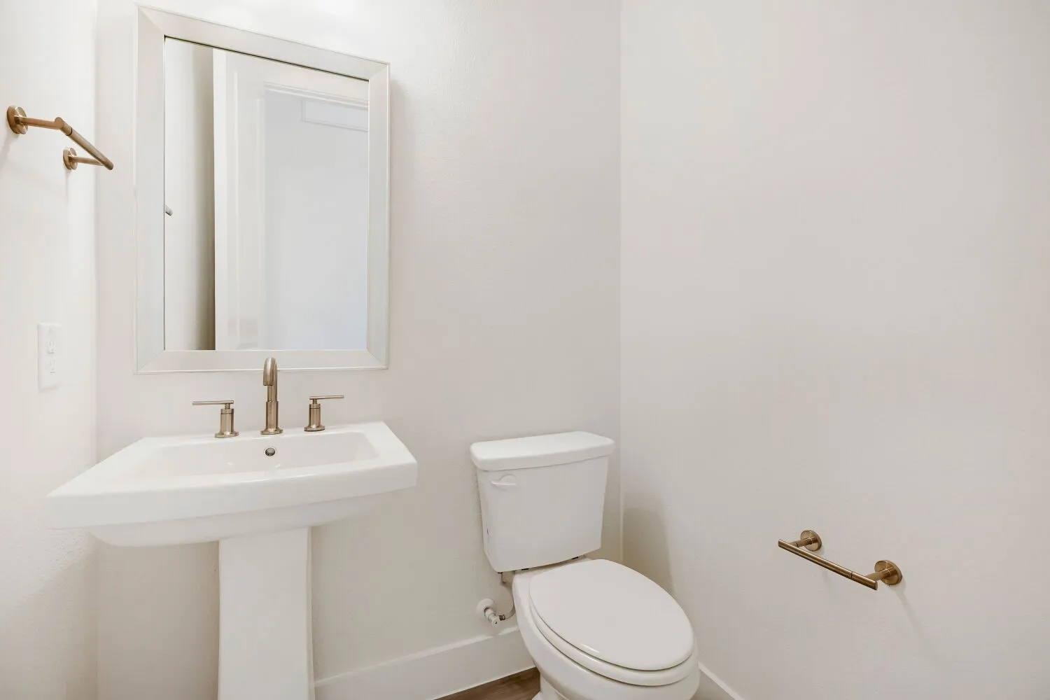 White pedestal sink with brushed nickel faucet, framed mirror, and coordinating bronze hardware