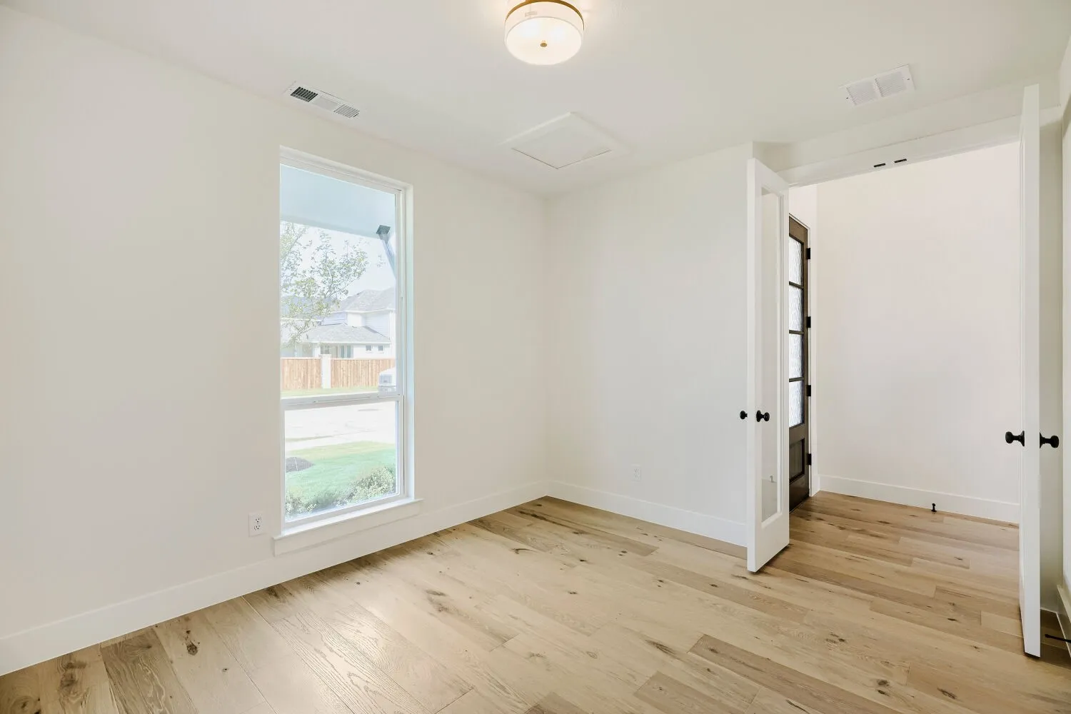 Bright room featuring wood-finish flooring, a large vertical window, white walls, and a contemporary ceiling light fixture