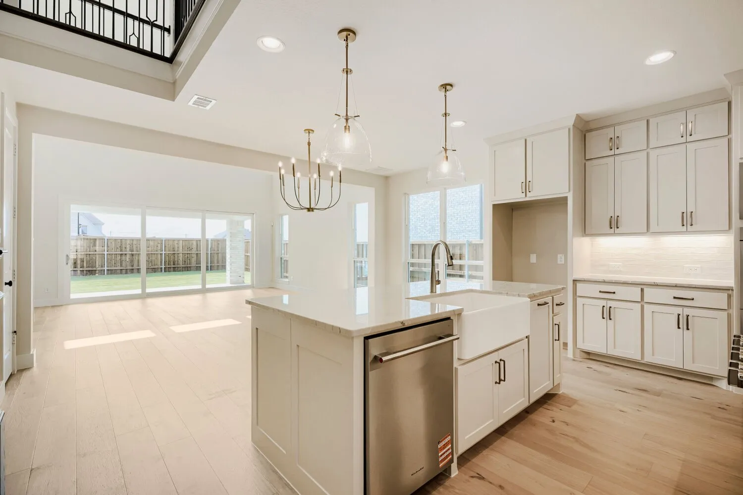 Open-concept kitchen and living area featuring light wood-finish flooring, a kitchen island with a farmhouse sink, stainless steel dishwasher, and quartz countertops