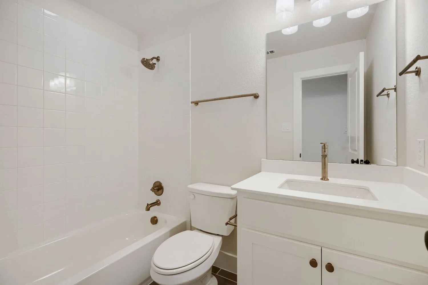 Bathroom featuring a white subway tile tub surround, white vanity with an integrated sink, vanity mirror, bronze-finish fixtures, and dark tile flooring
