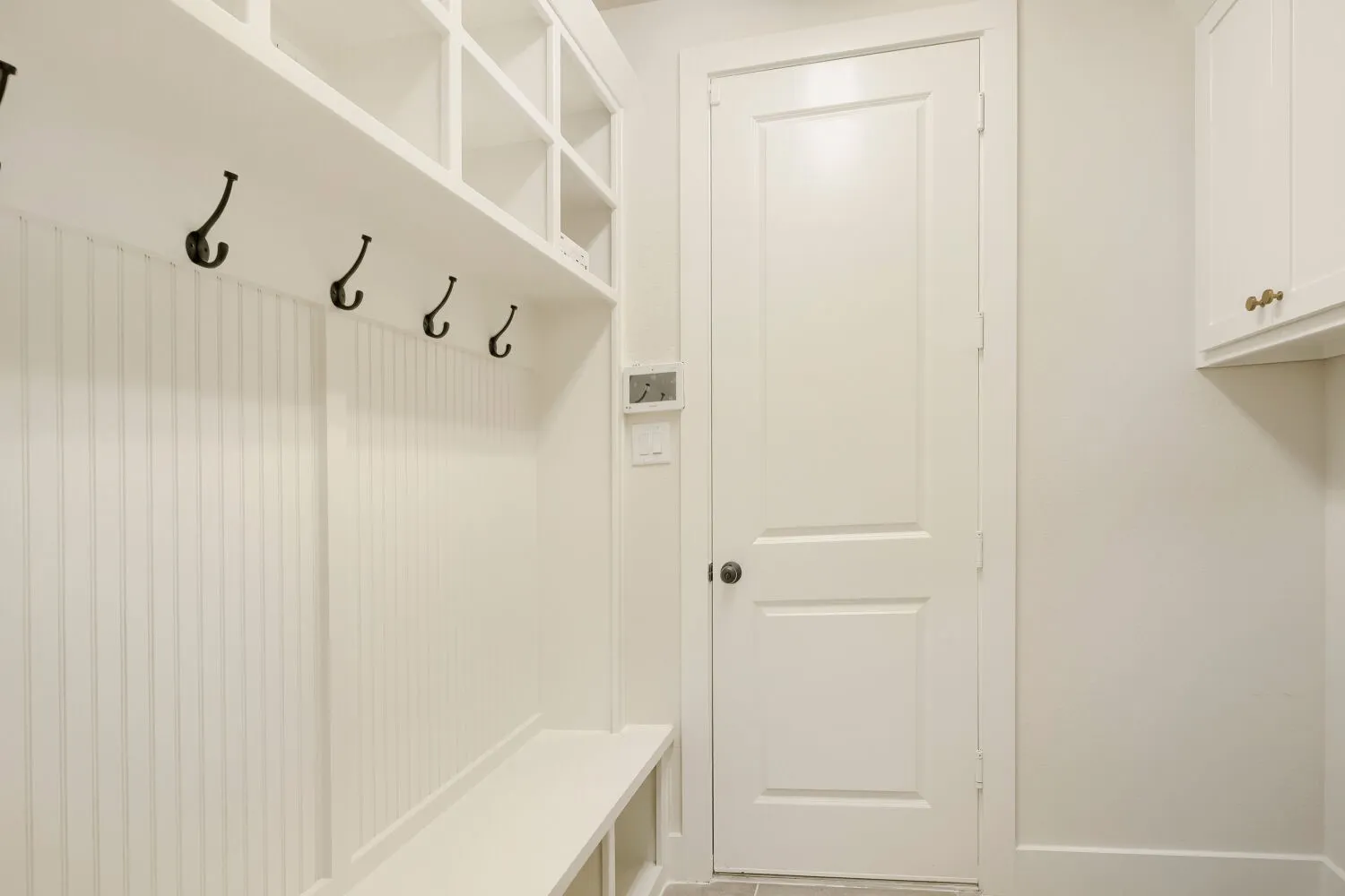 Built-in mudroom bench with cubby storage, beadboard paneling, and five black coat hooks