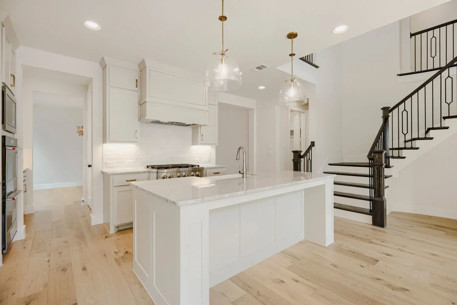 Modern kitchen featuring a large central island with a sink, white cabinetry with gold hardware, stainless steel appliances, and a tile backsplash