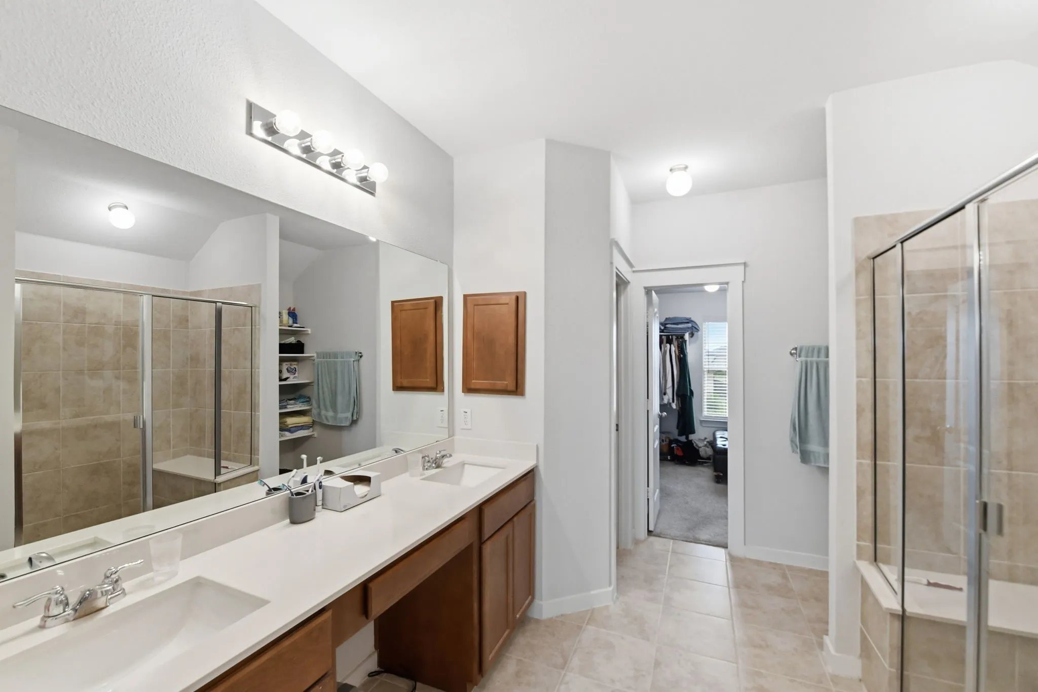 Mstr Bathroom with a shower stall, double vanity, light tile patterned flooring, and a walk in closet