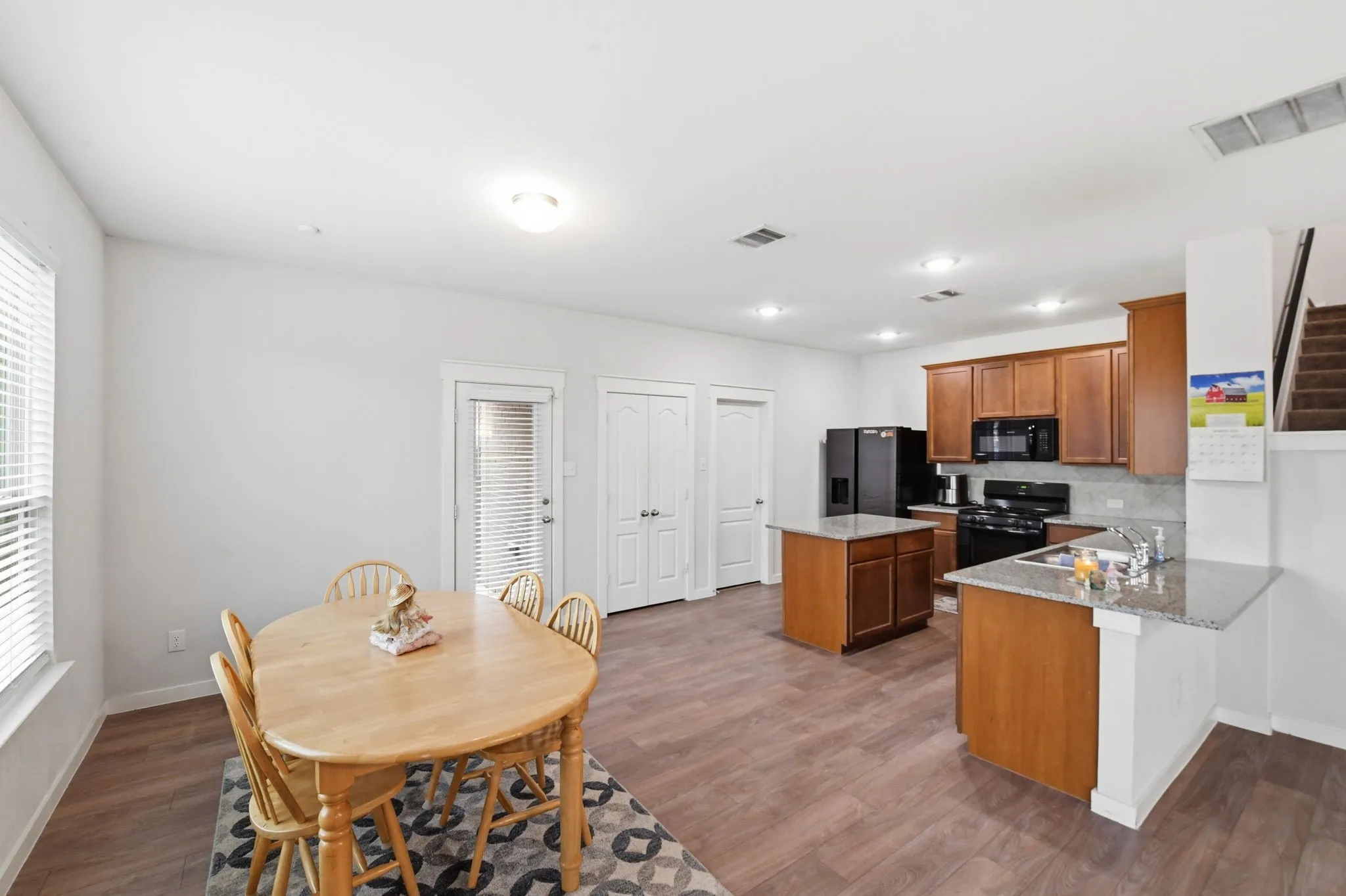 Kitchen featuring wood finish cabinets, black appliances, dark wood-style floors, a peninsula, and light stone counters