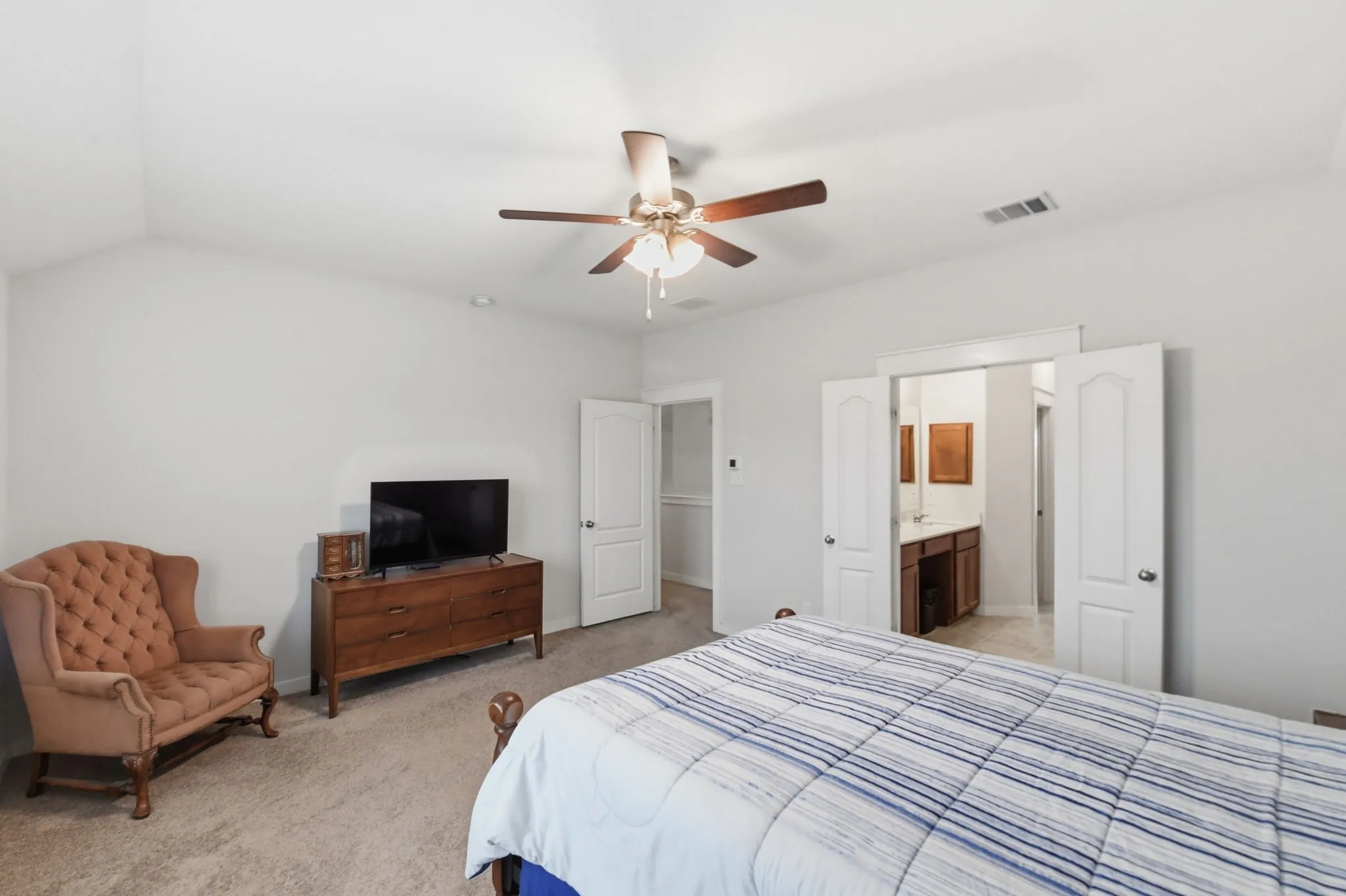 Bedroom featuring light colored carpet, a ceiling fan, connected bathroom, and vaulted ceiling