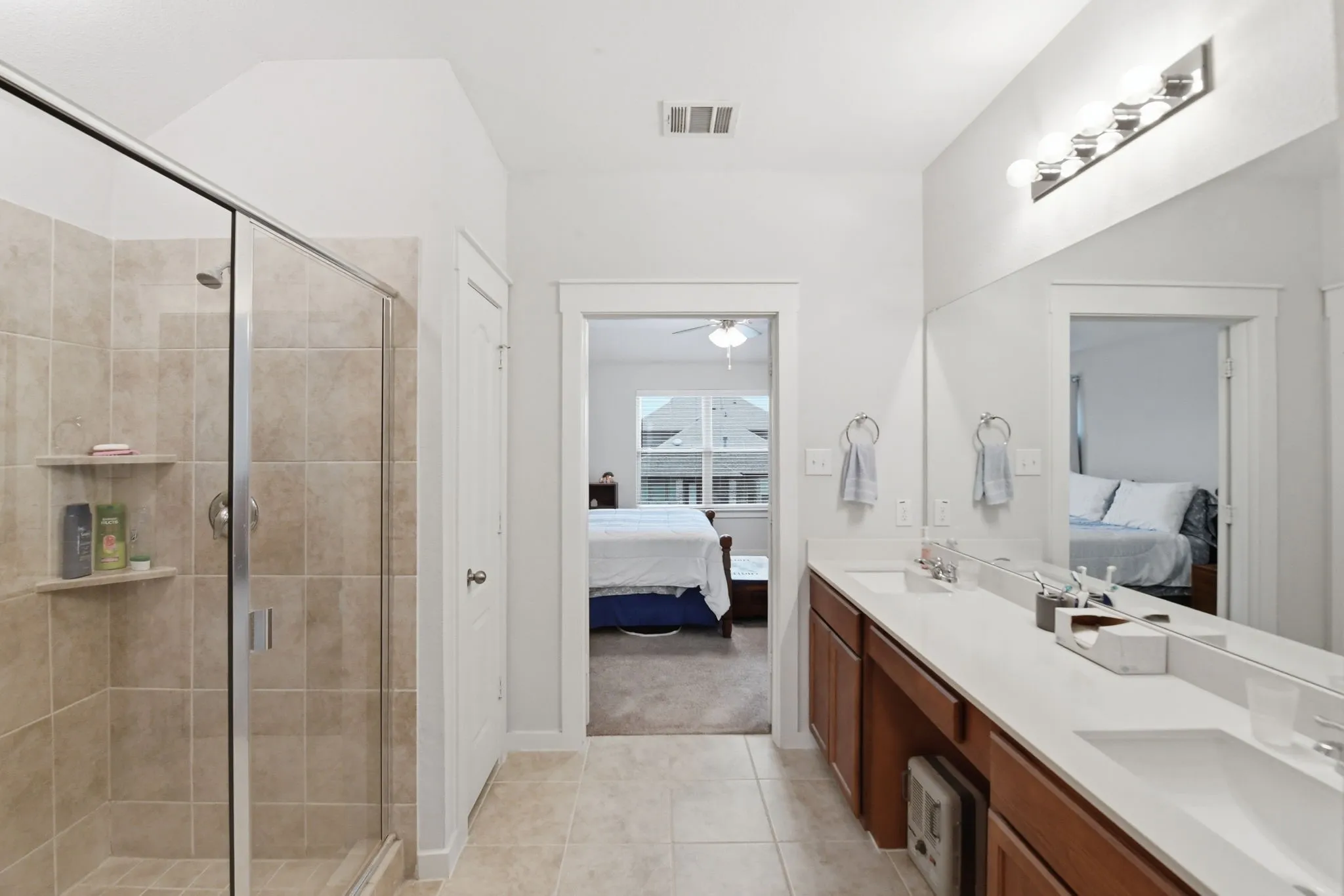 Ensuite bathroom with double vanity, a stall shower, light tile patterned flooring, and light colored carpet