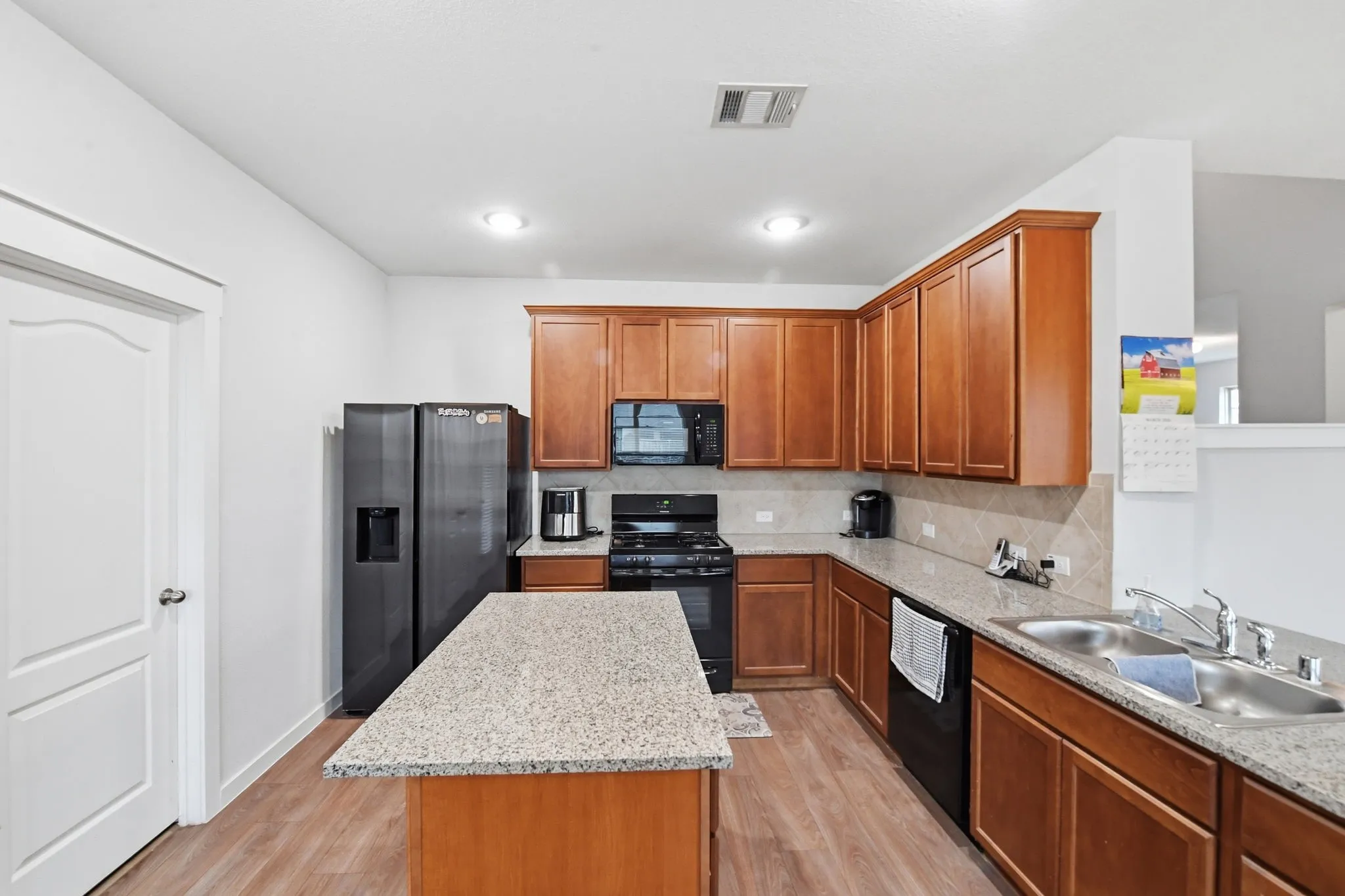 Kitchen with a center island, black appliances, wood finish cabinets, light wood-type flooring, and backsplash