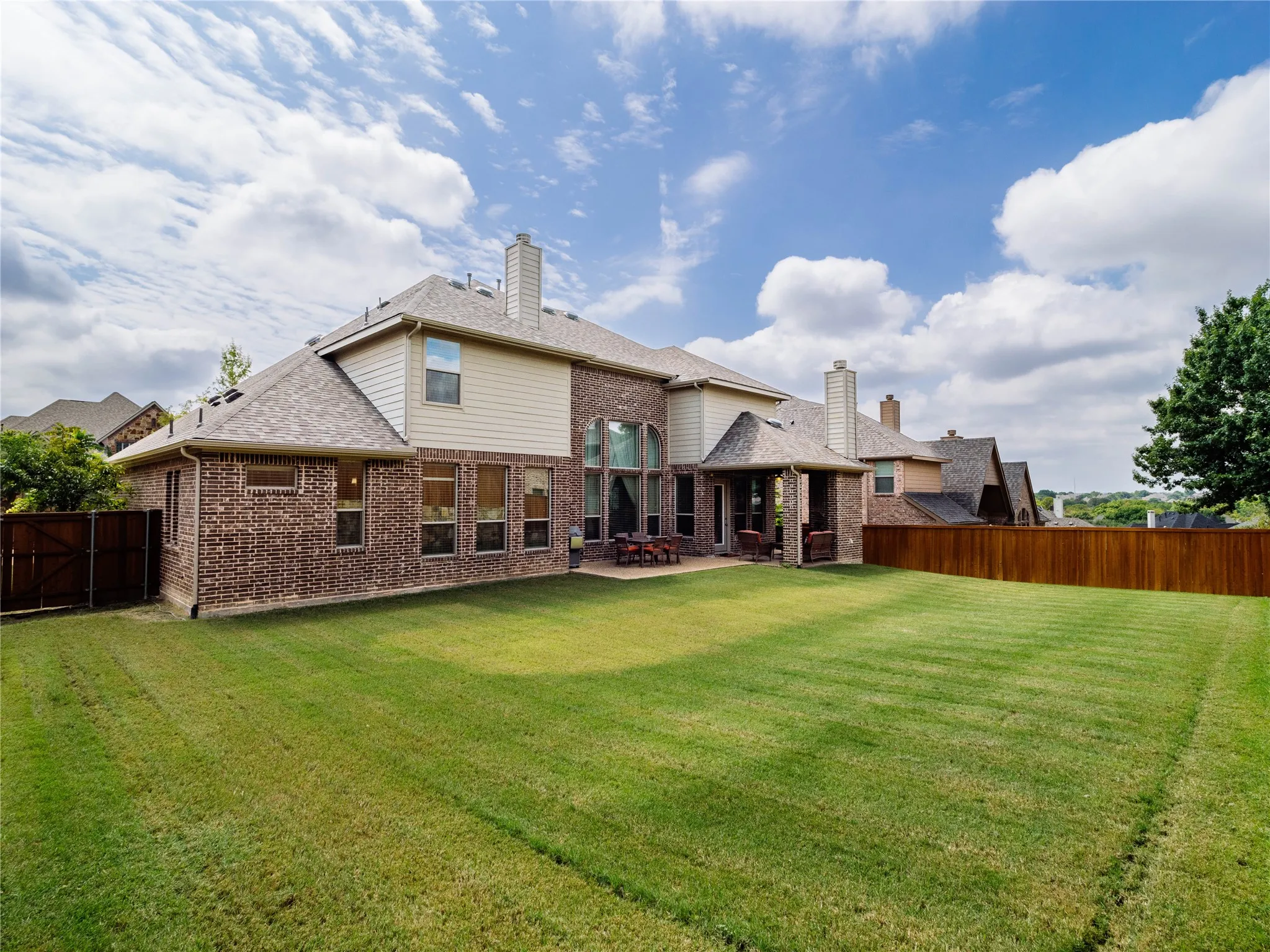 Back of house featuring brick siding, a fenced backyard, a patio area, a chimney, and roof with shingles