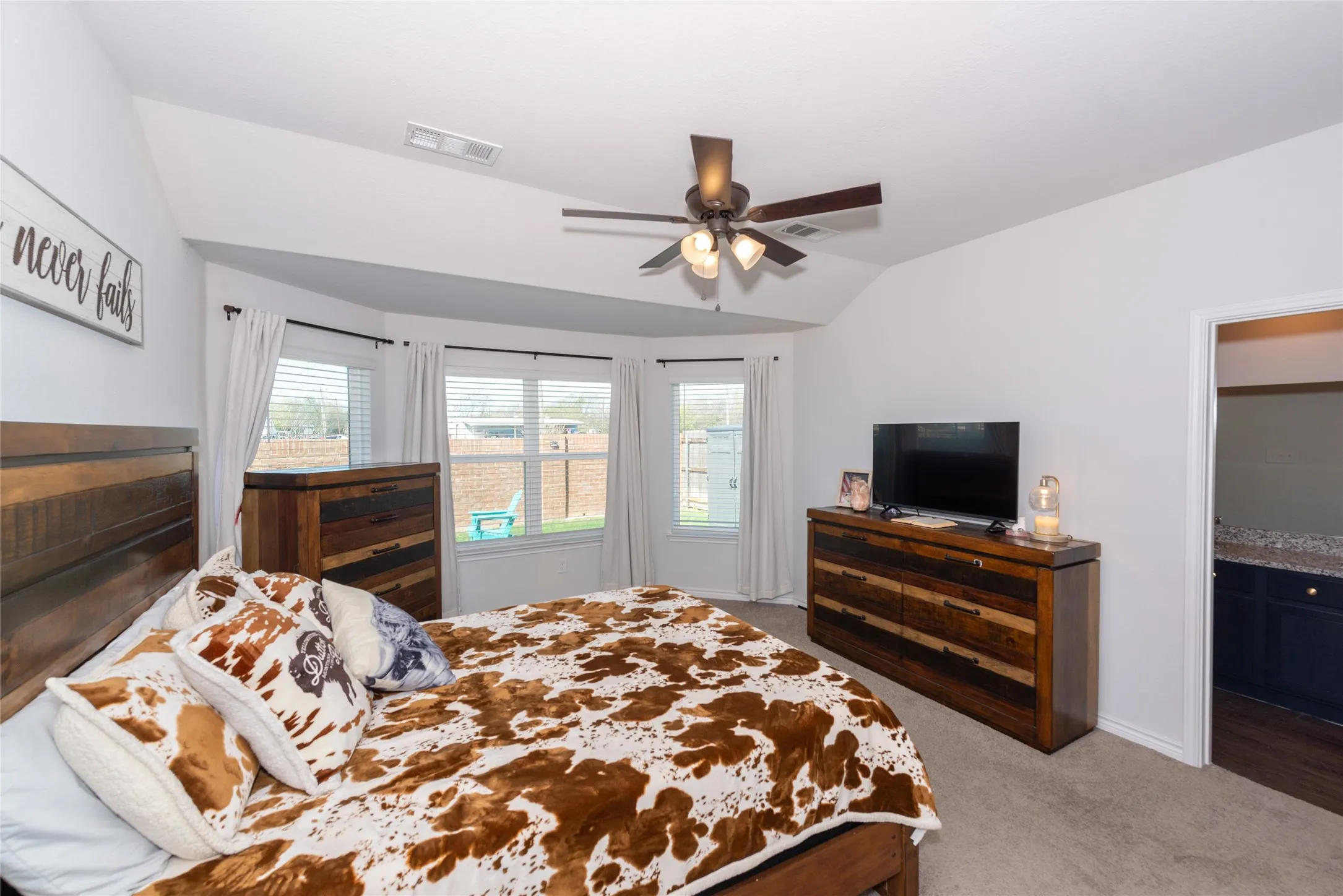 Bedroom featuring vaulted ceiling, dark carpet, ceiling fan, and ensuite bath