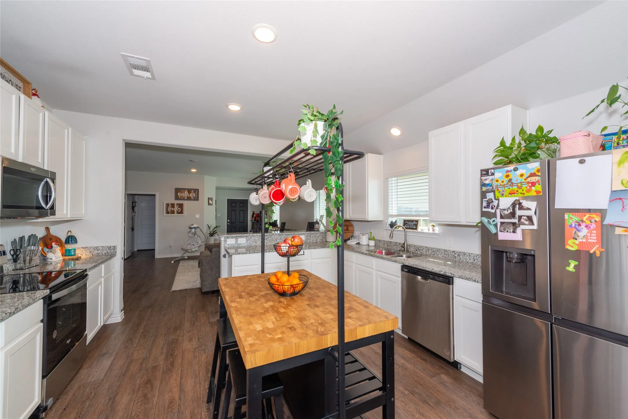 Kitchen with stainless steel appliances, white cabinets, light stone counters, dark wood finished floors, and recessed lighting