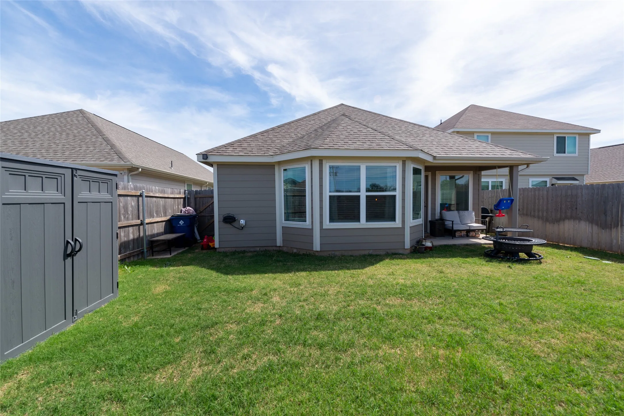 Rear view of property with a patio, a fenced backyard, a fire pit, a shingled roof, and a shed