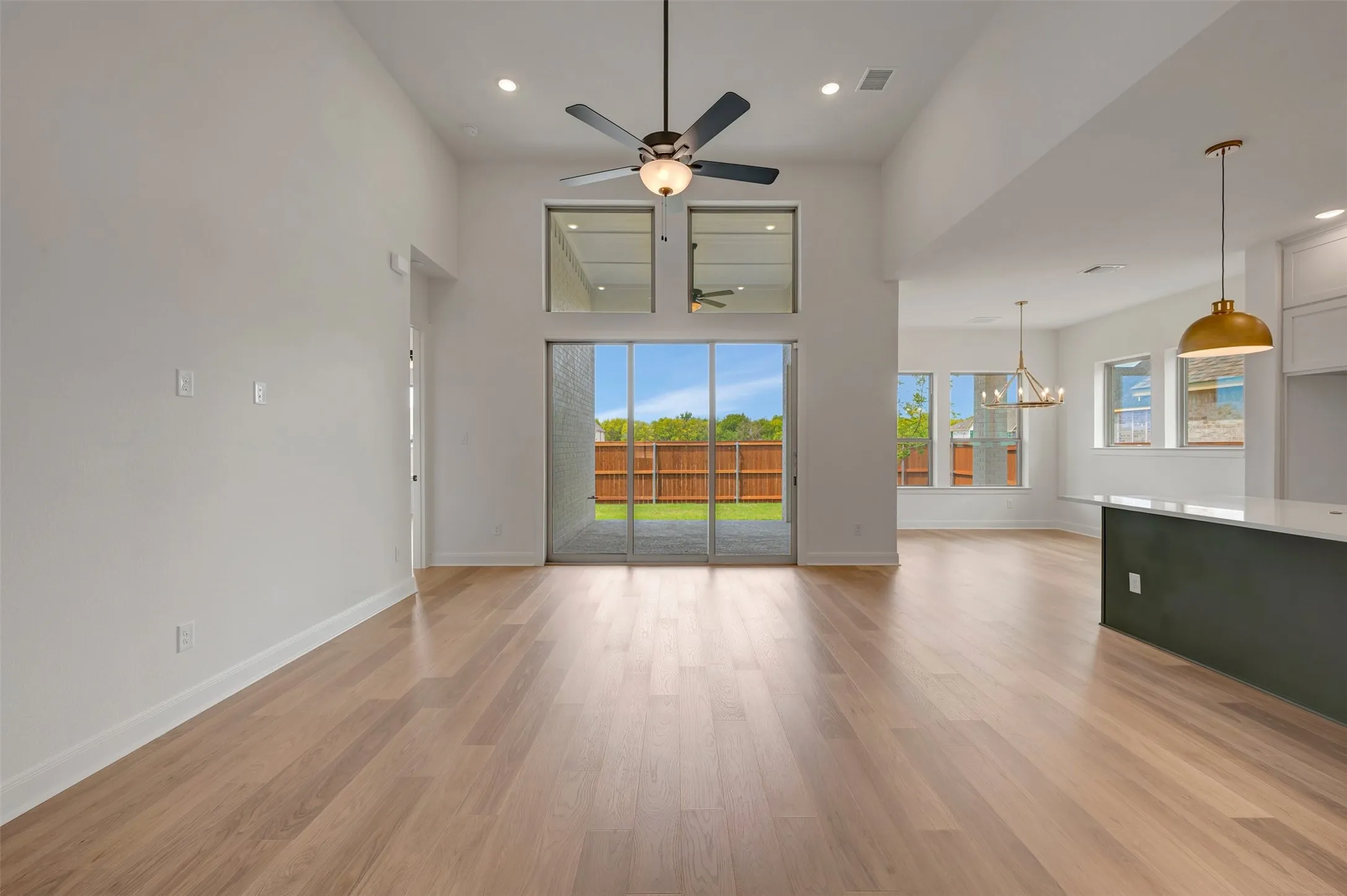 Vaulted ceilings, wood-finish flooring, sliding glass patio doors, kitchen island with a light-toned countertop, and recessed lighting