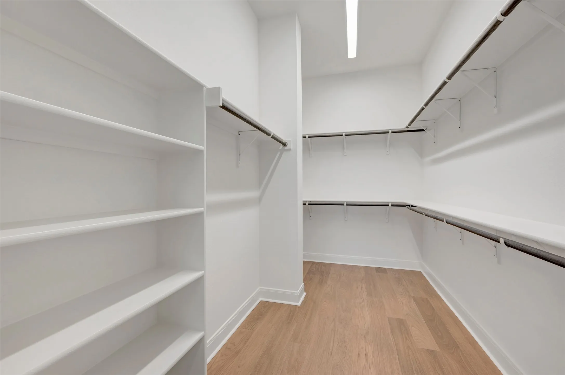 Expansive walk-in closet featuring wood-finish flooring, extensive built-in shelving, multiple hanging rods, and recessed lighting