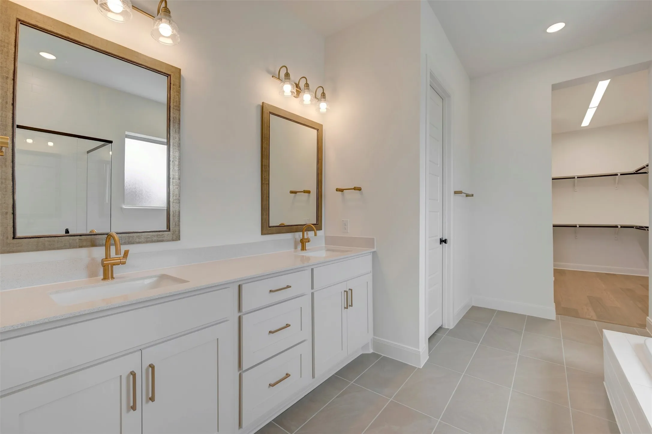 Dual vanity with gold-finish fixtures, white cabinetry, integrated sinks, and individual mirrors