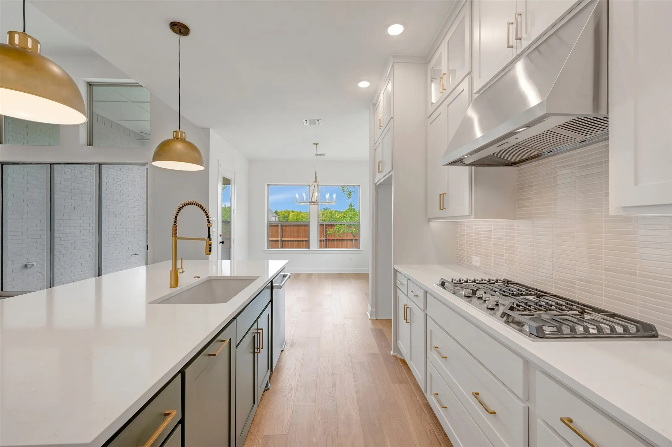 Contemporary kitchen featuring a gas range, stainless steel range hood, light-toned cabinetry, and a central island with an undermount sink and golden-finish faucet