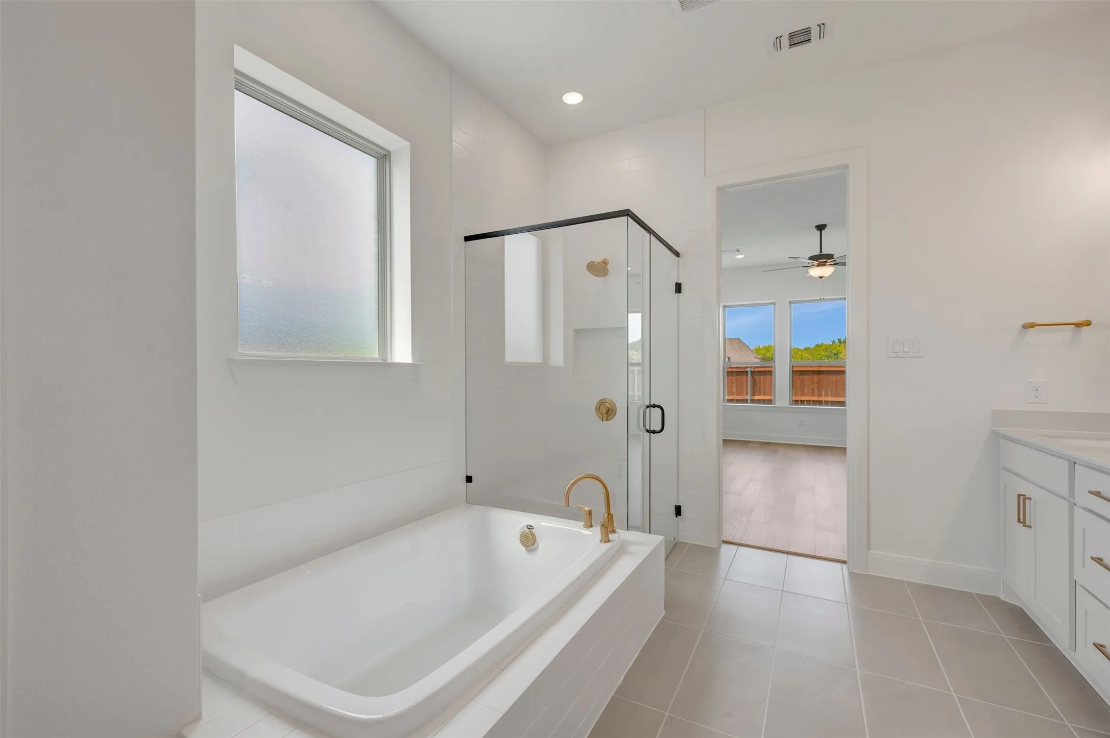 Soaking tub with brass-finish faucet, glass-enclosed shower with black trim, single vanity with white cabinetry, and tile flooring