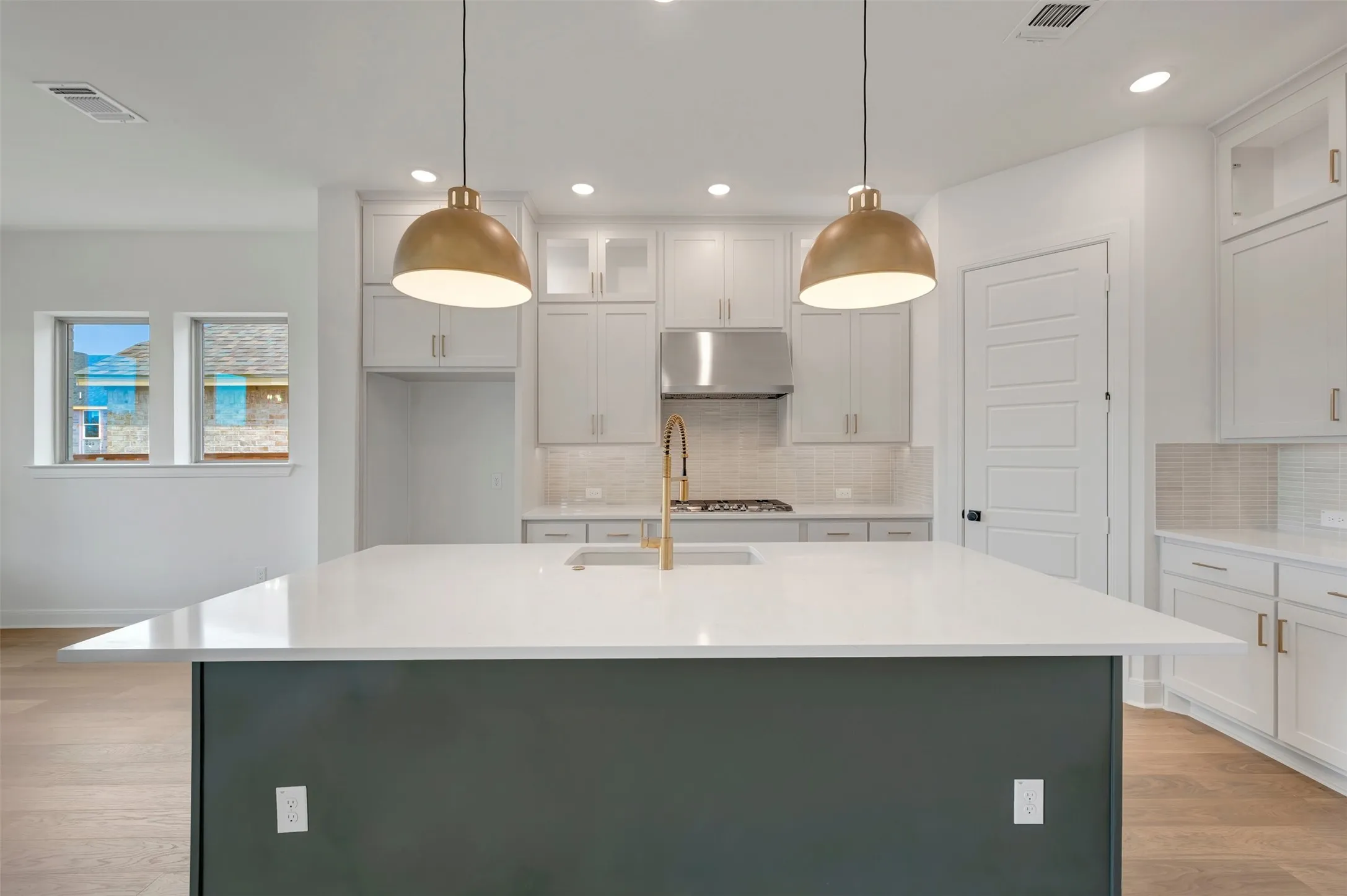 Kitchen featuring a large central island with a light-toned countertop, pendant lighting, white cabinetry, and stainless steel appliances