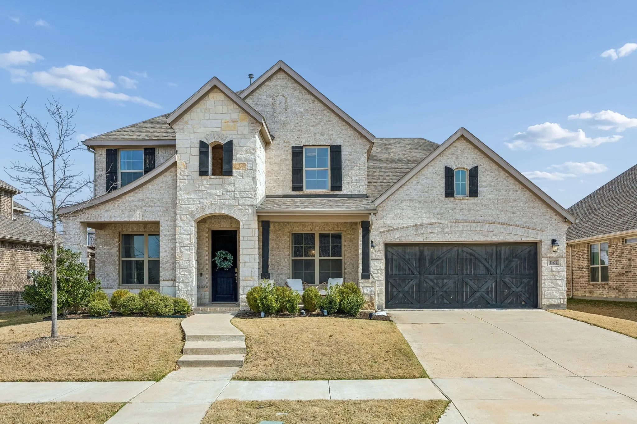French country home featuring a porch, stone siding, driveway, and brick siding