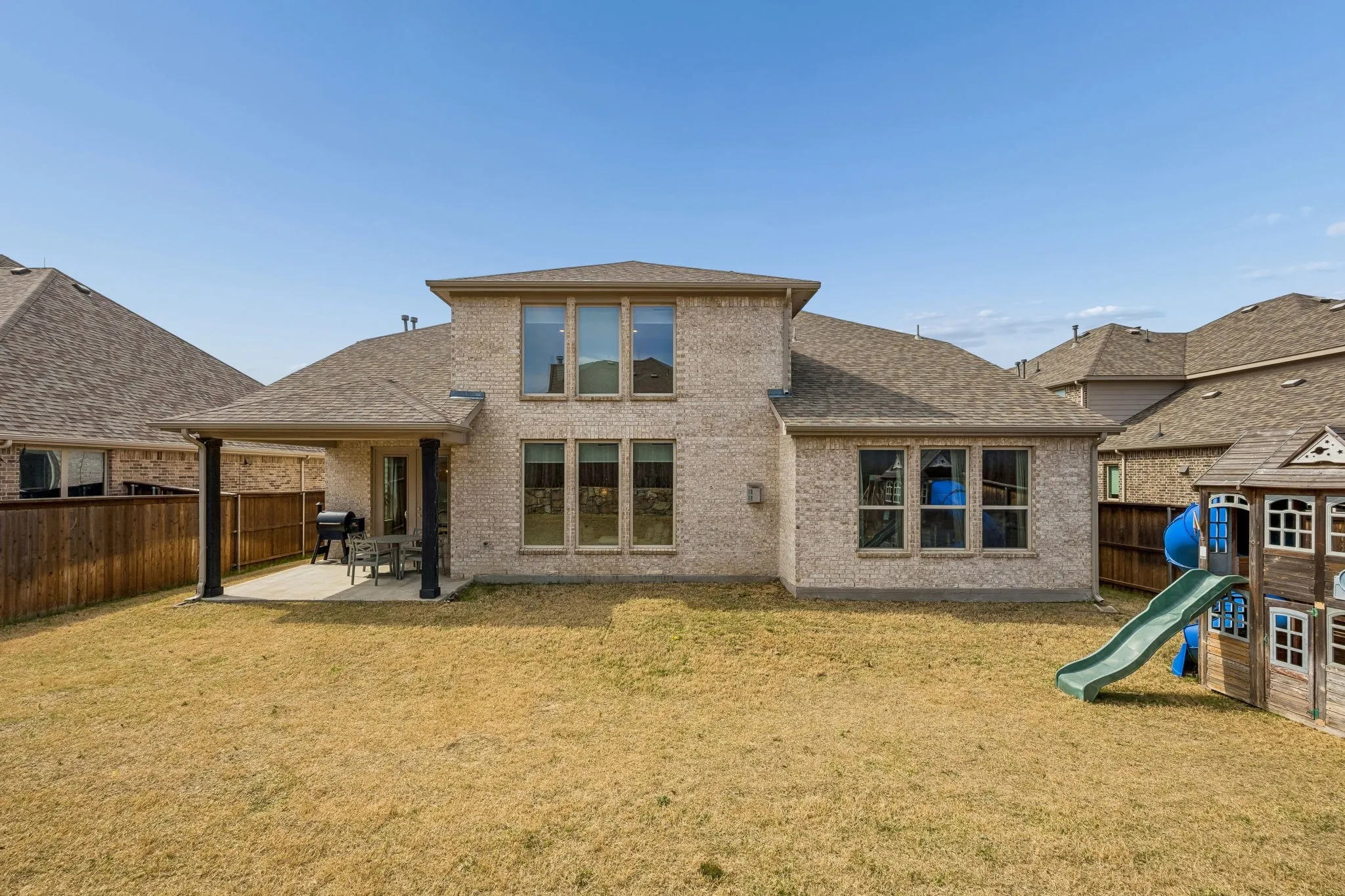 Rear view of house with a patio area, roof with shingles, a fenced backyard, brick siding, and a playground