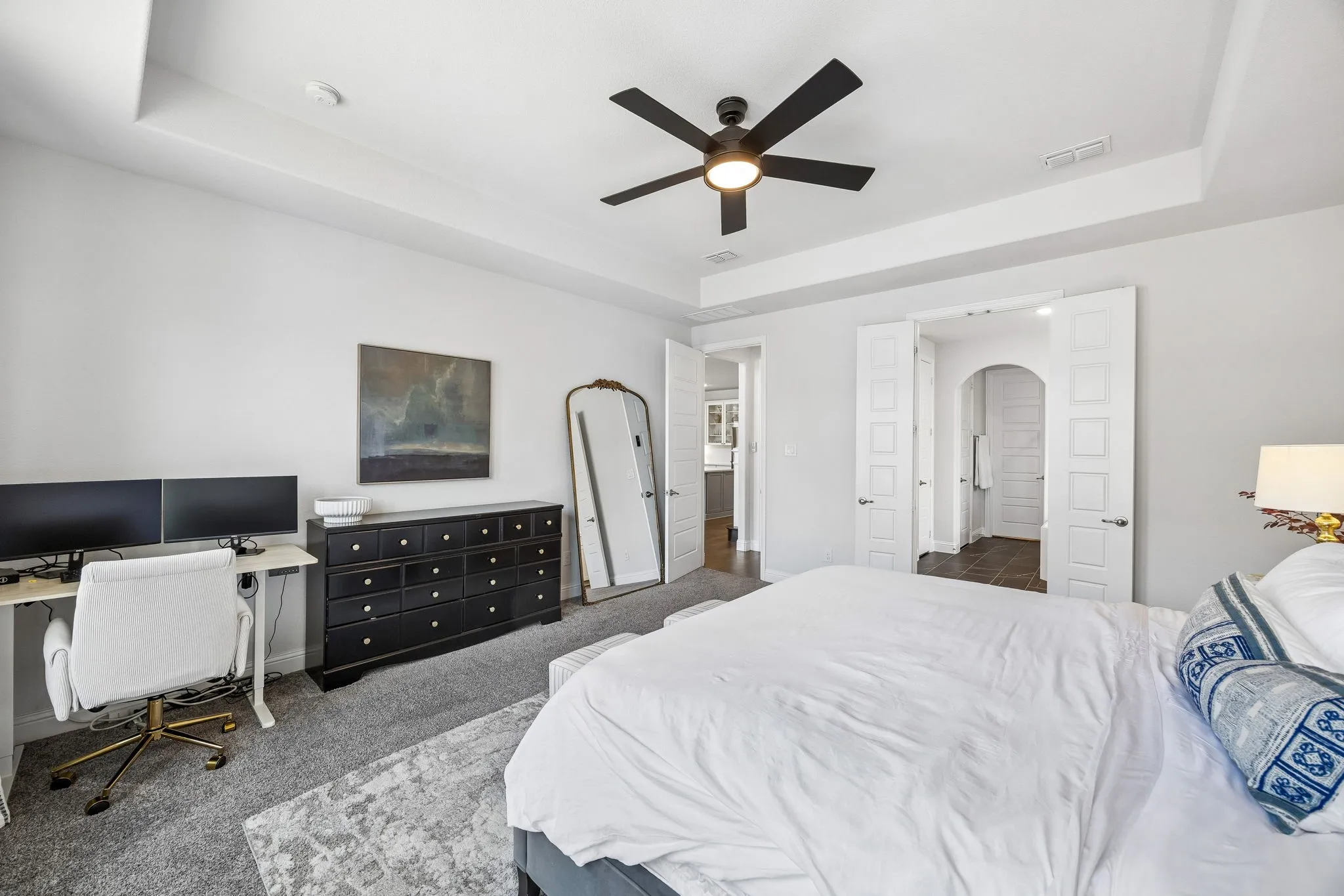 Bedroom featuring a tray ceiling, dark colored carpet, ceiling fan, a desk, and arched walkways