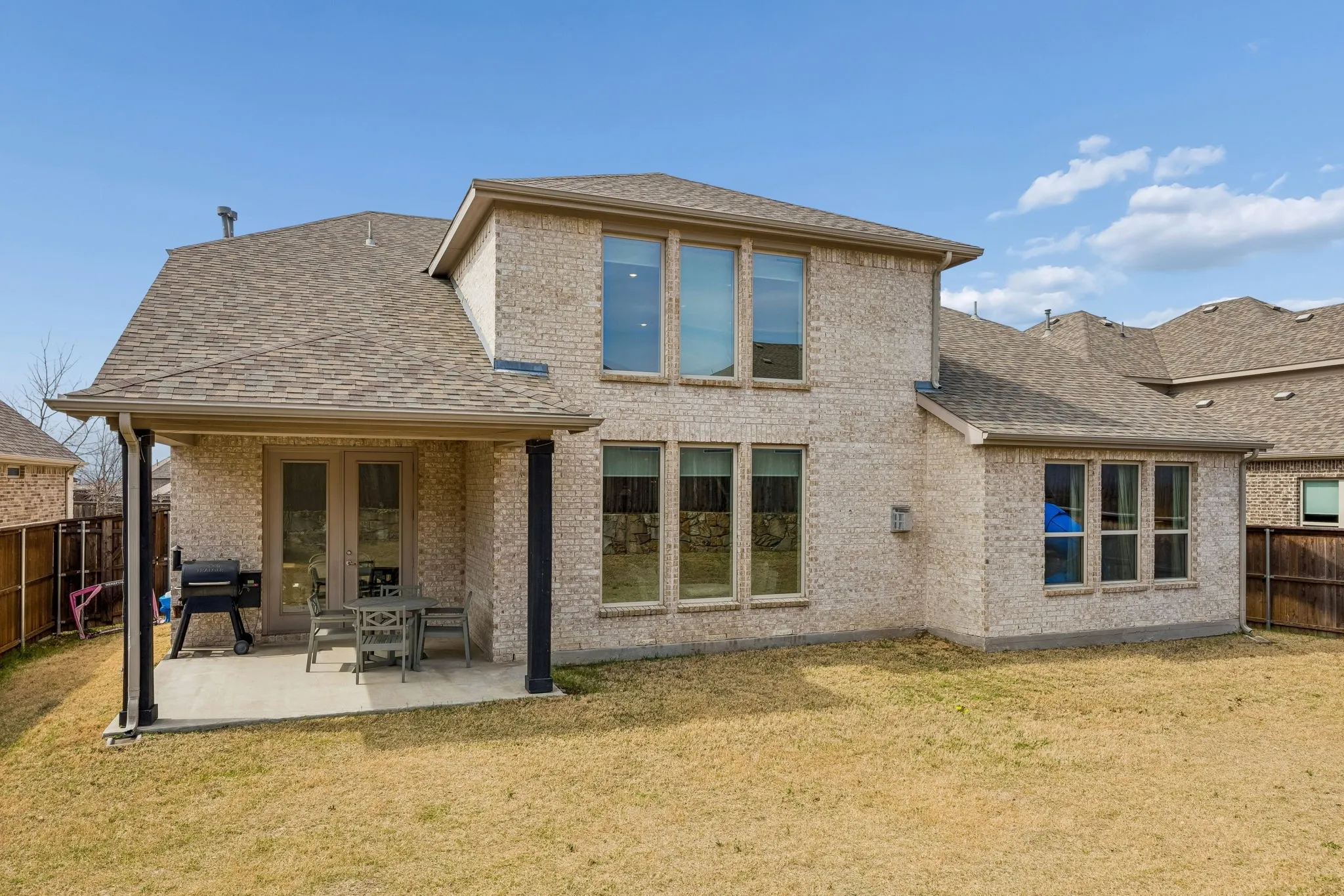 Rear view of property featuring a fenced backyard, a patio area, roof with shingles, and brick siding