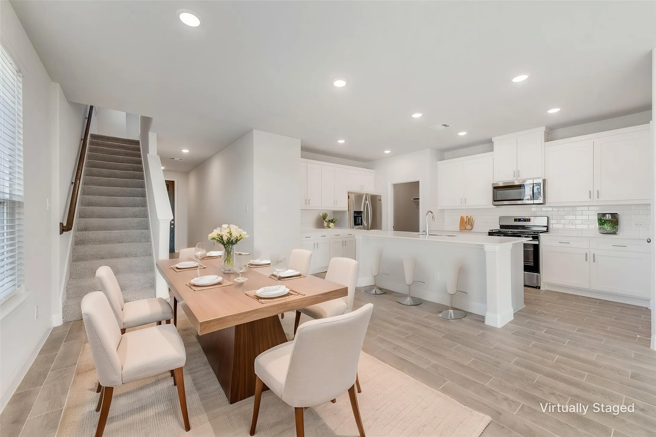 Open-concept living area featuring a kitchen with white cabinetry and stainless steel appliances, a center island with seating, a designated dining area, and wood-finish flooring
