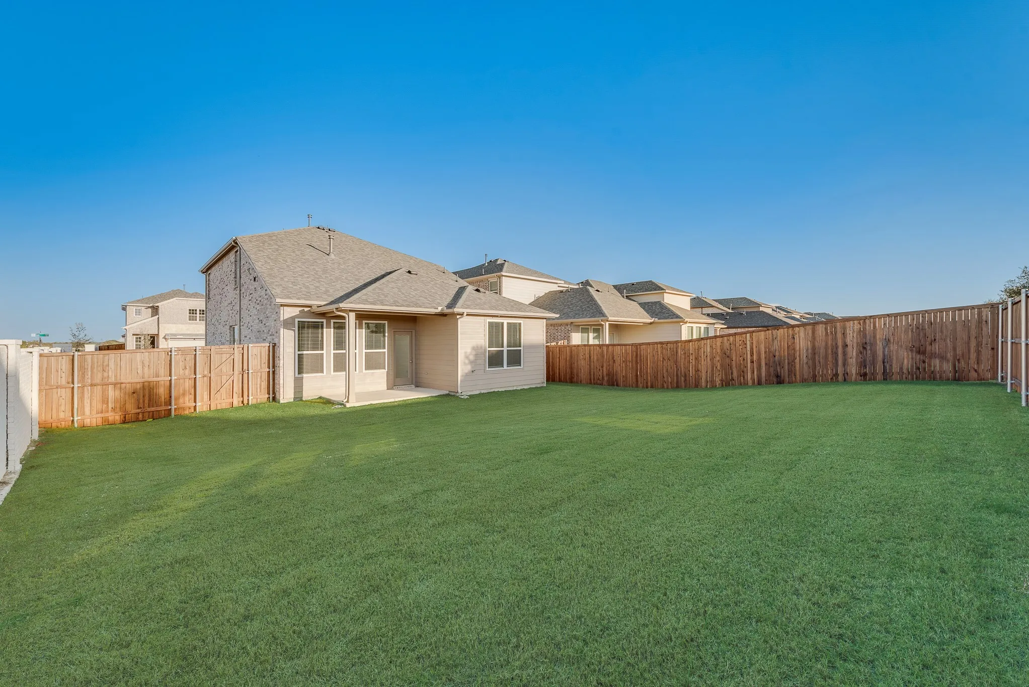 Expansive backyard with a large grass lawn, surrounded by a wooden privacy fence, and featuring a concrete patio