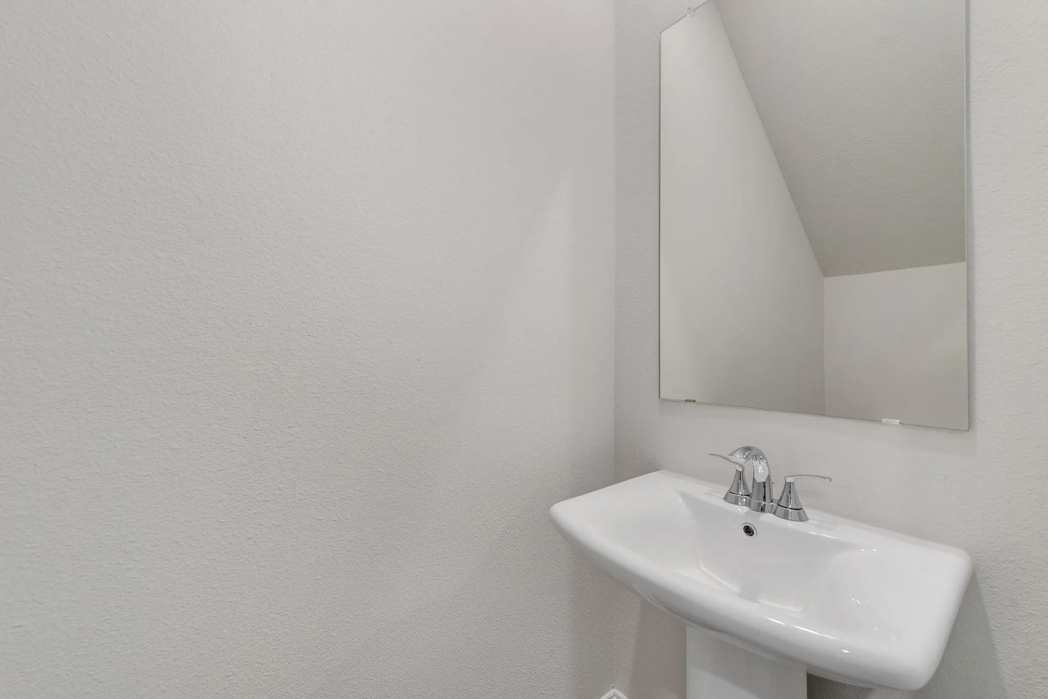 Pedestal sink with a chrome faucet and a frameless rectangular mirror