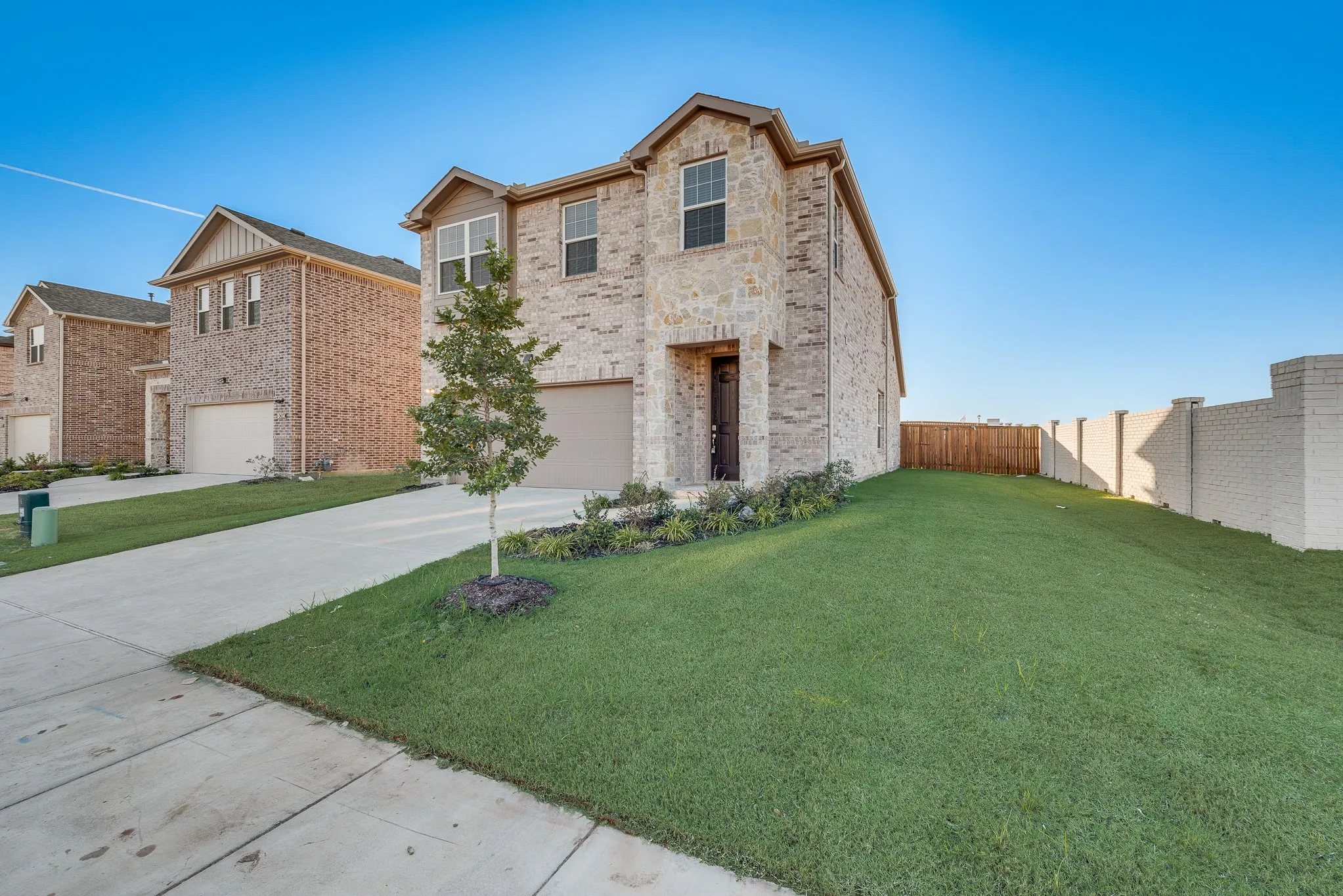 Two-story residence featuring a brick and stone facade, attached garage, concrete driveway, and a partially fenced backyard with a brick privacy wall
